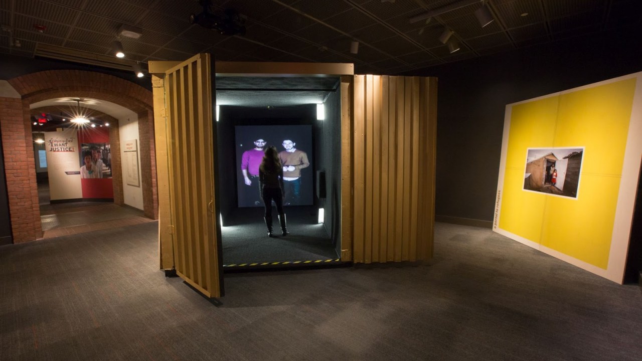 Image of a shipping container with a video portal at the far end of it and a person inside talking to two other people from the portal