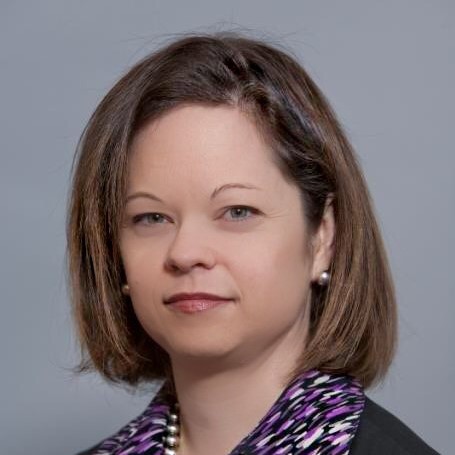 Headshot of a woman with shoulder length brown hair smiling slightly at the camera head tilted slightly to the left.