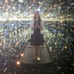 A woman stands in a Kusama installation and takes a selfie.