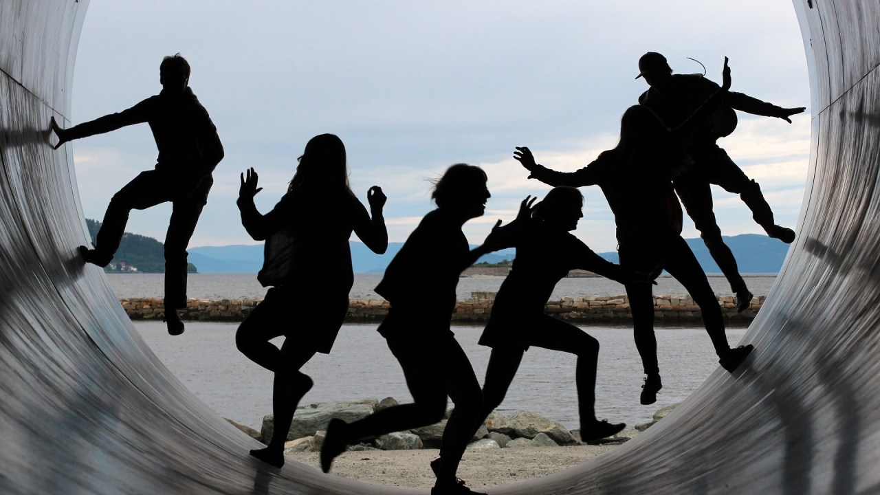 A shadowy group of individuals jump and play in a very large circular tube.