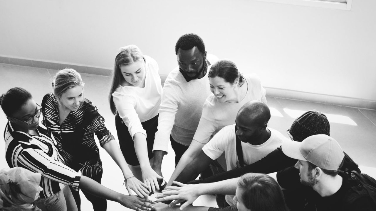 A black-and-white photo of a group joining hands in a circle, an expression of teamwork.