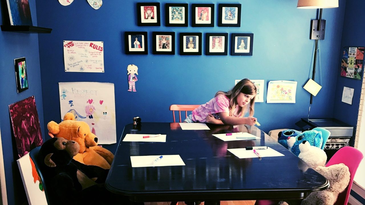 A child is seen sitting around a table with stuffed animals seated in chairs.