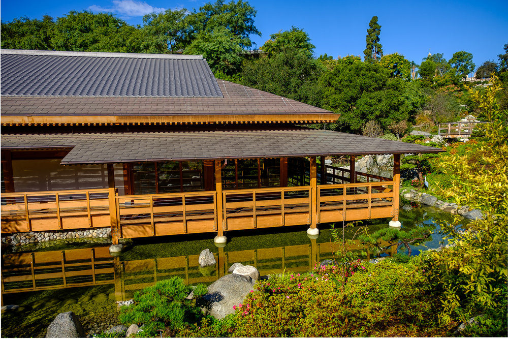 Exterior shot of a Japanese-style building surrounded by trees and gardens.