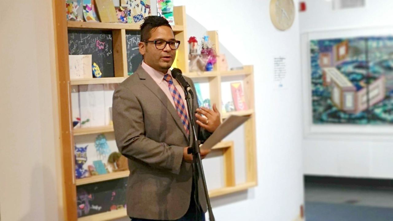 David Rios speaking at a microphone inside of a children's museum space.