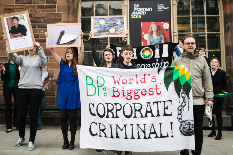 A group of individuals stand with protest signs the largest of which says, "BP: World's Biggest Corporate Criminal!"