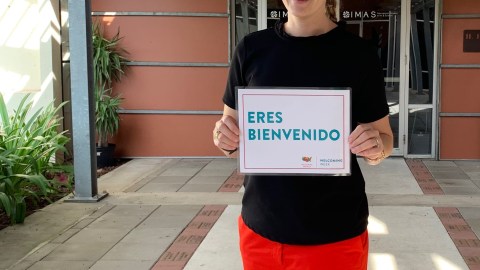 A person stands at the front entrance of the museum holding up a sign that says "ERES BIENVENIDO."