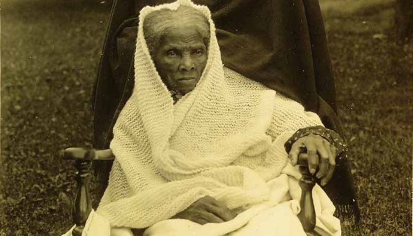 Harriet Tubman sits in a wheelchair wrapped in a knitted blanket.