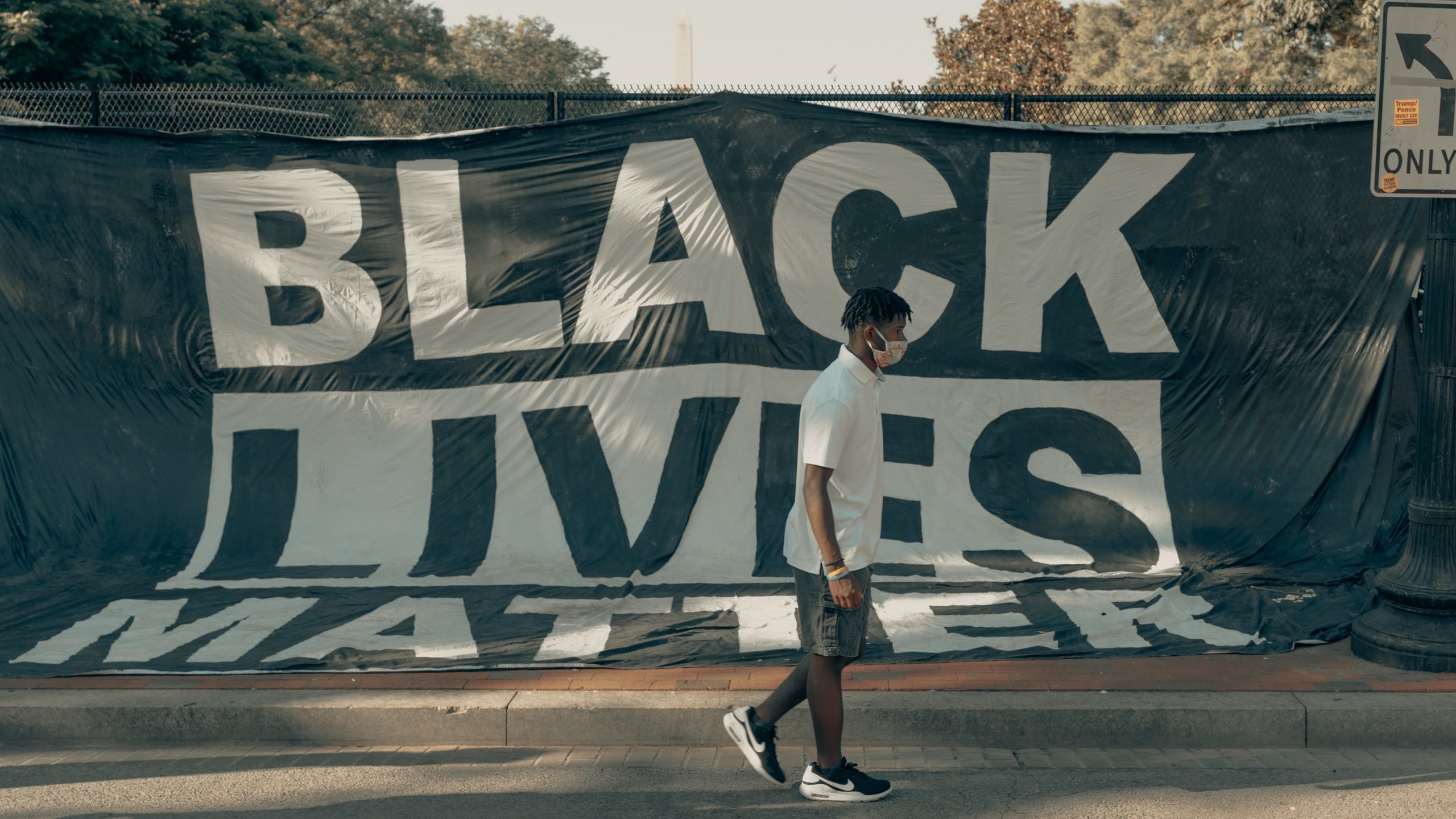 A teenager wearing a face mask walking past a Black Lives Matter banner hung on a fence