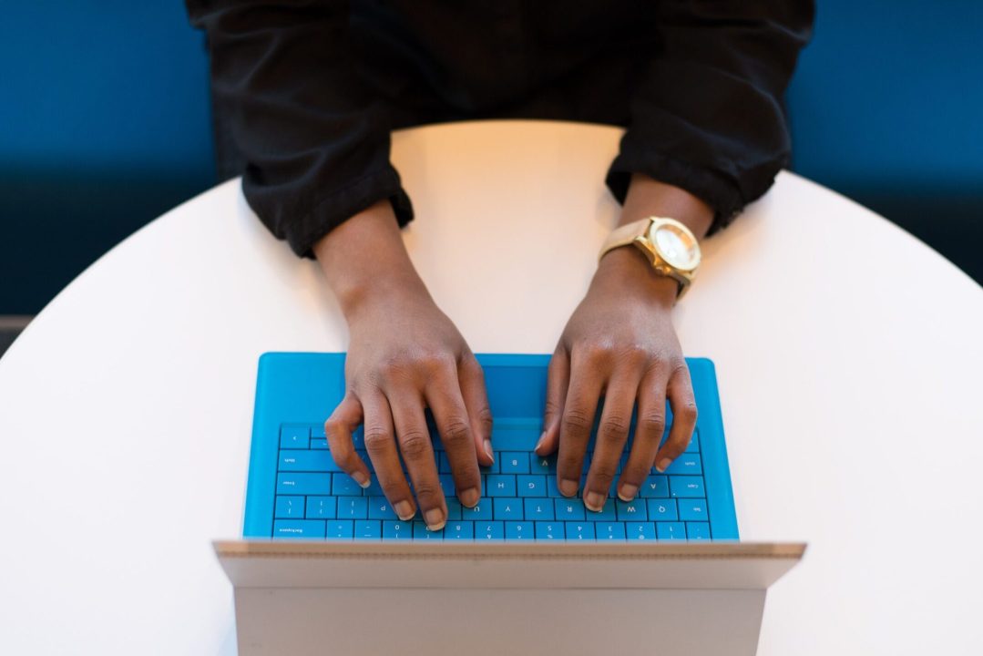 a person seen from above typing on a laptop with a blue keyboard