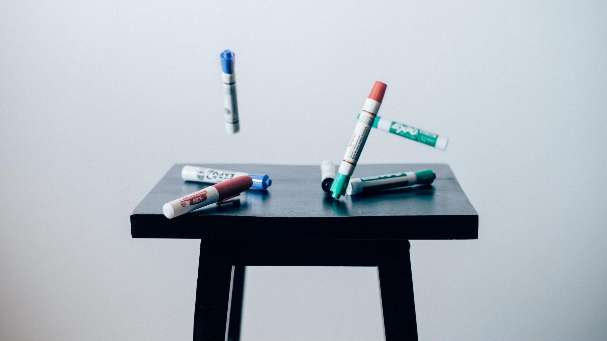 A black stool with dry erase markers mid-air above it