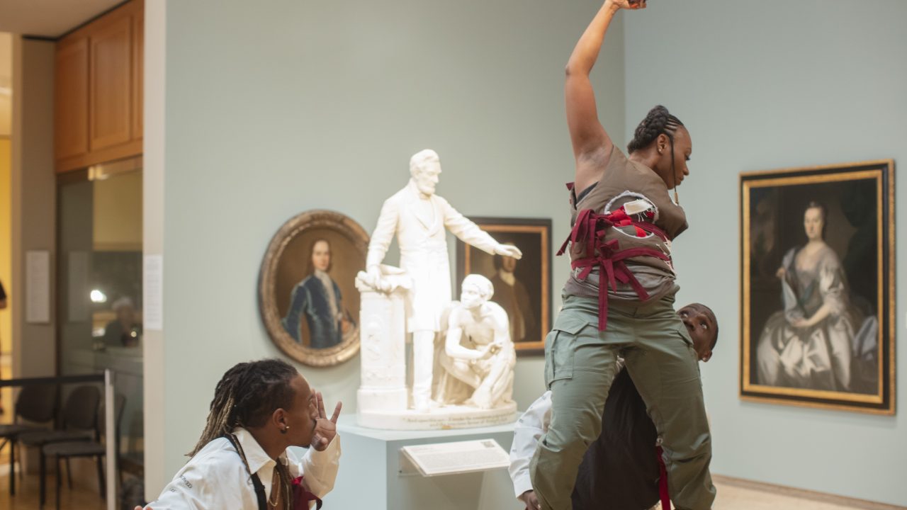 Dancers performing around a sculpture of Abraham Lincoln and an enslaved person in a museum gallery