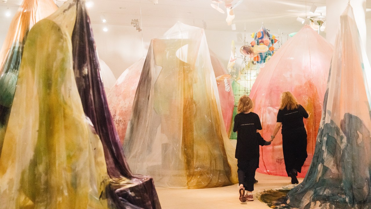 Three people walking through an installation with sculptures consisting of draped painted textiles