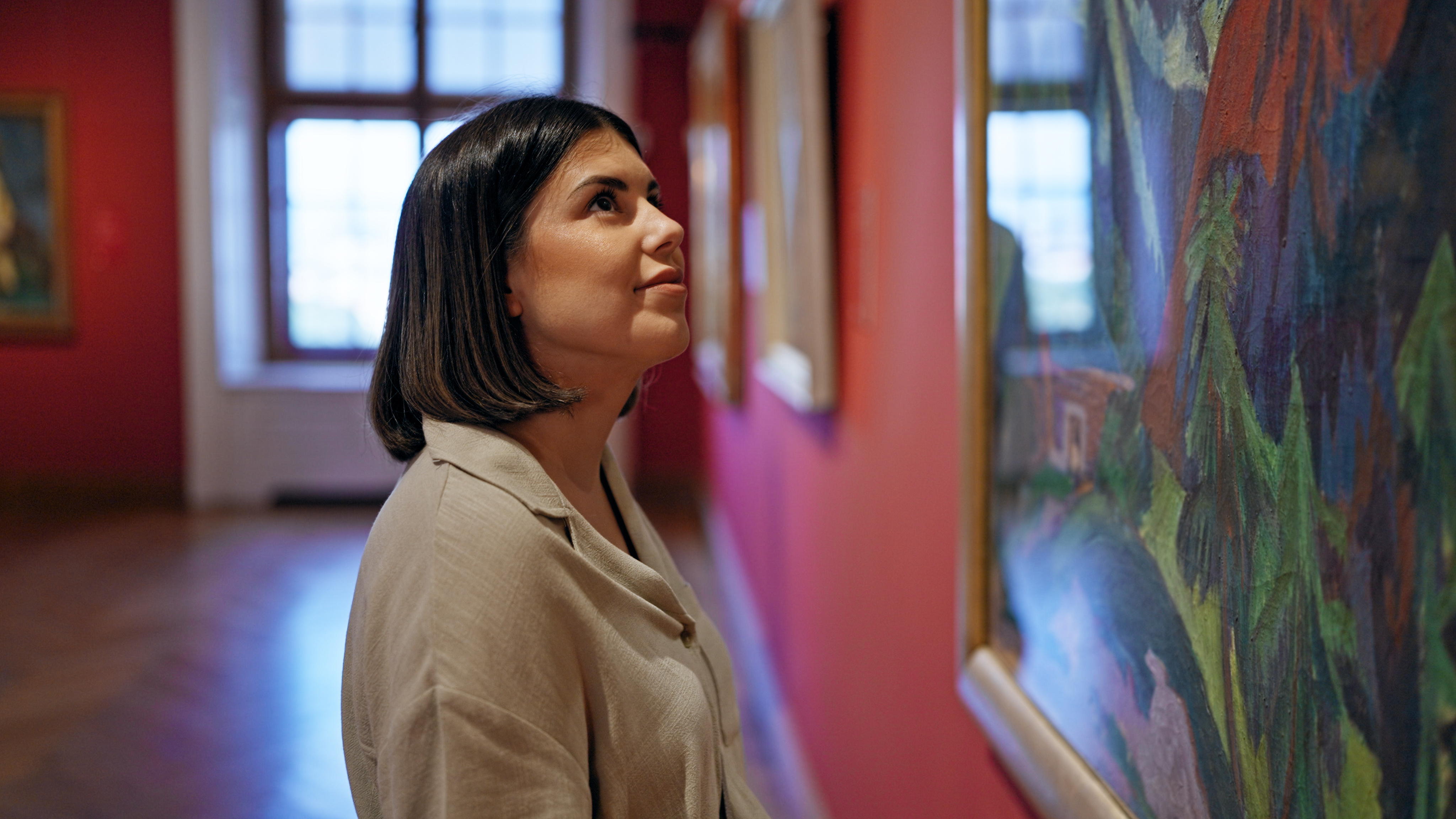 A person admiring a colorful painting in an art gallery.