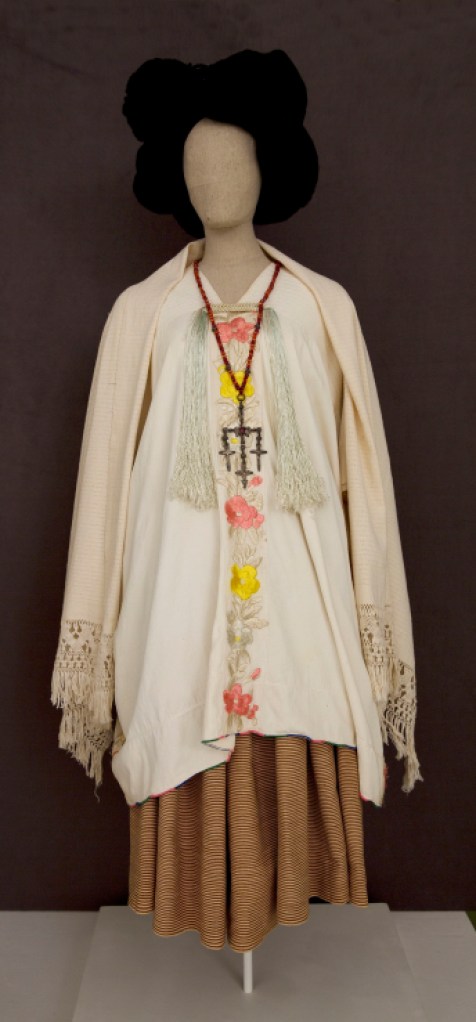 A mannequin wears an long sleeve white top with embroidered buttons and a long brown skirt. 