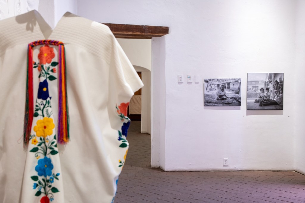 The back of an embroidered shirt on a mannequin stands to the left with a couple of framed photographs hanging on a wall in the distance. 