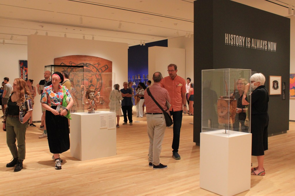 Visitors inside an exhibition with a title wall reading "History is Always Now."