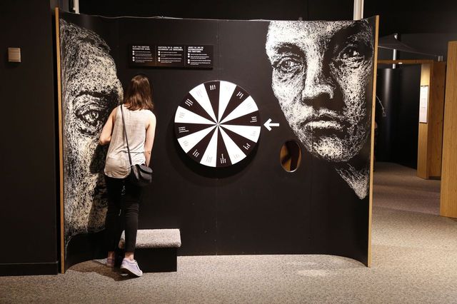 A woman stands looking closely at an exhibit panel with various interactive elements.