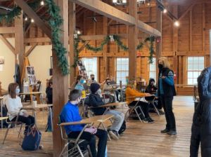 A group of students sit at desks while an instructor teaches before them. 