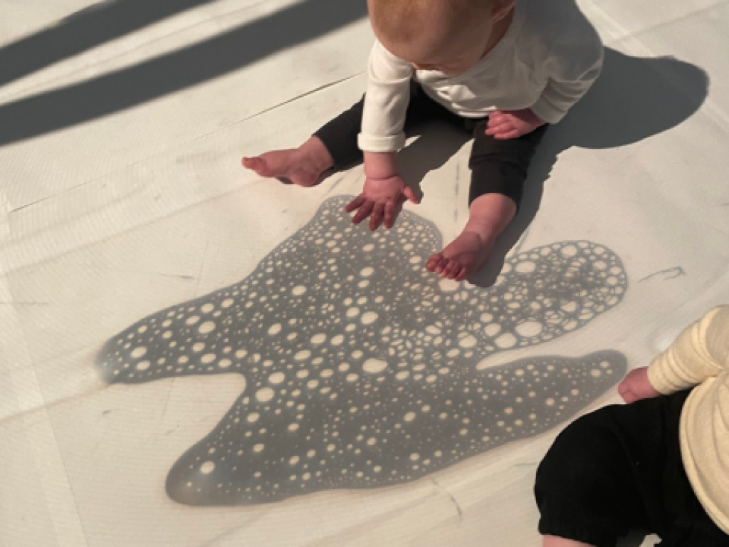 A baby explores and interacts with a shadow projection on the ground