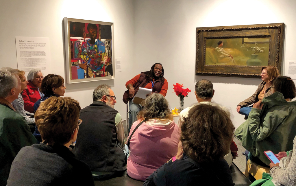 A group of people seated around a speaker between two paintings in a museum gallery