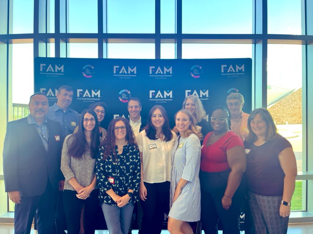 A group shot of people in front of a backdrop with the logo of the First Americans Museum