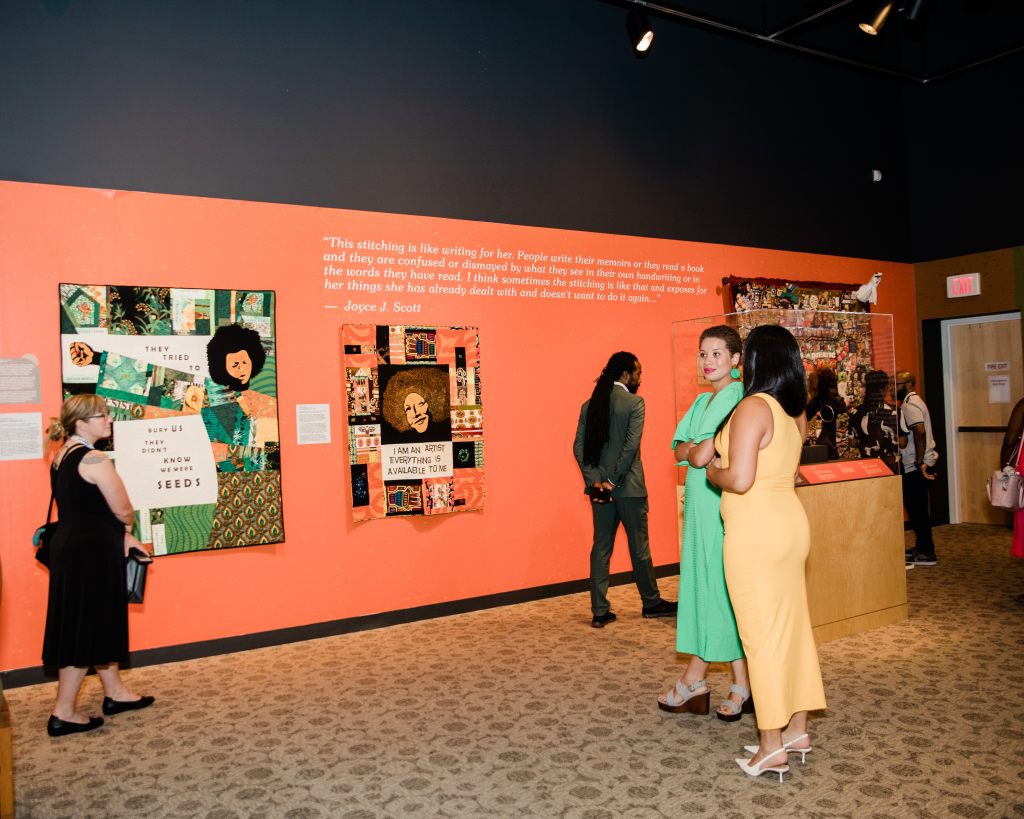 People browsing a museum gallery with collage style artworks by Joyce J. Scott