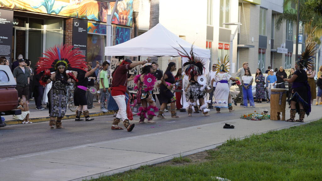 A troupe of performers in Indigenous dress dancing in front of the museum building