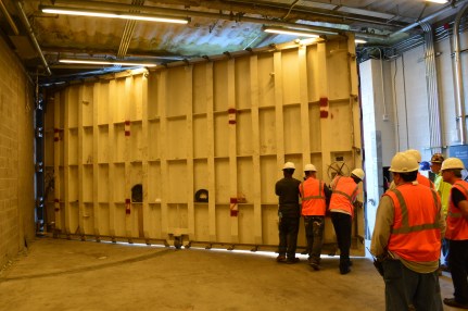 People wearing hard hats and construction vests close a large gate on a loading dock