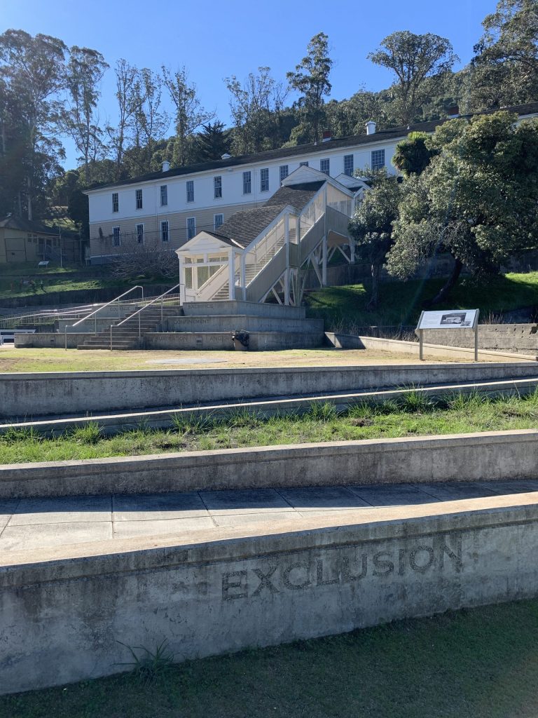 An exterior view of a two-story building with the word "Exclusion" engraved on a wall in front of it.