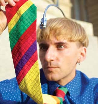 A man holds his multi-colored rainbow tie up while an antenna like apparatus extends from his head.