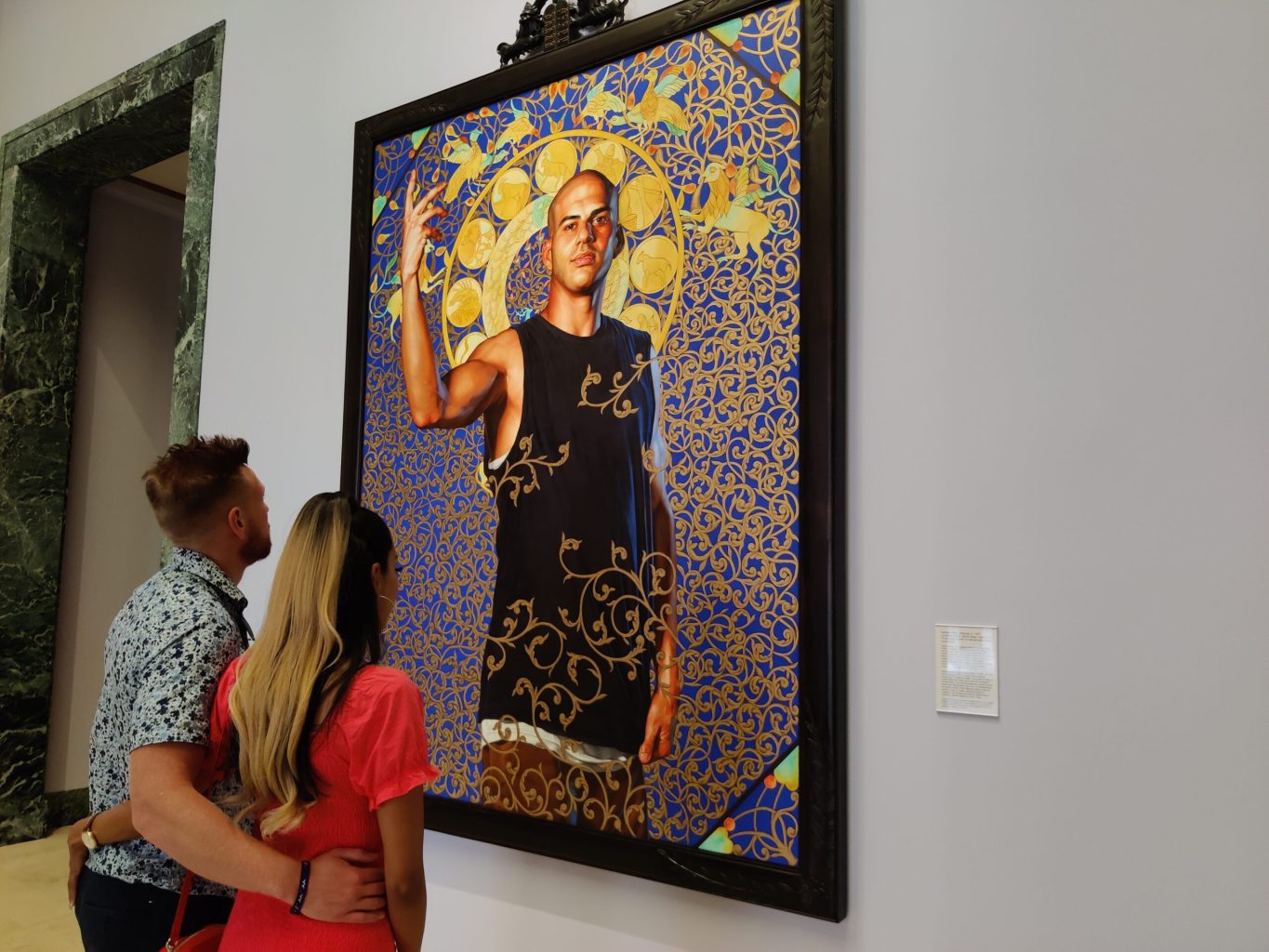 Visitors standing with their arms around each other looking at a painting of a subject surrounded by decorative spirals