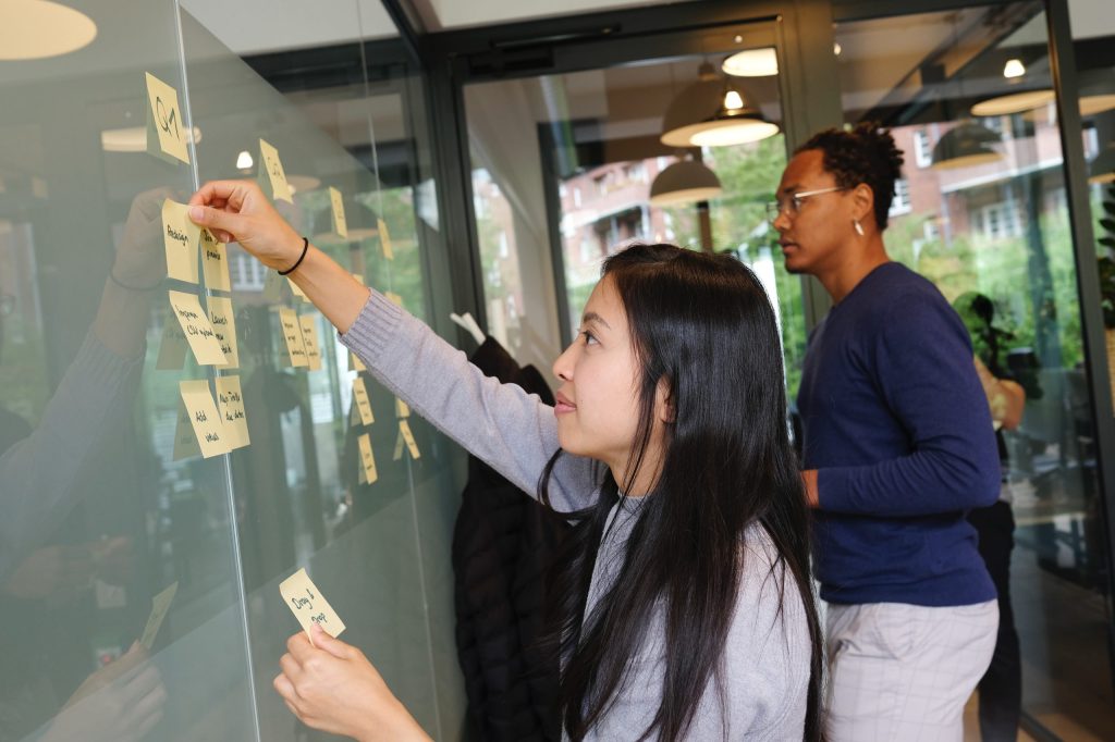 Two office workers pinning sticky notes to a board