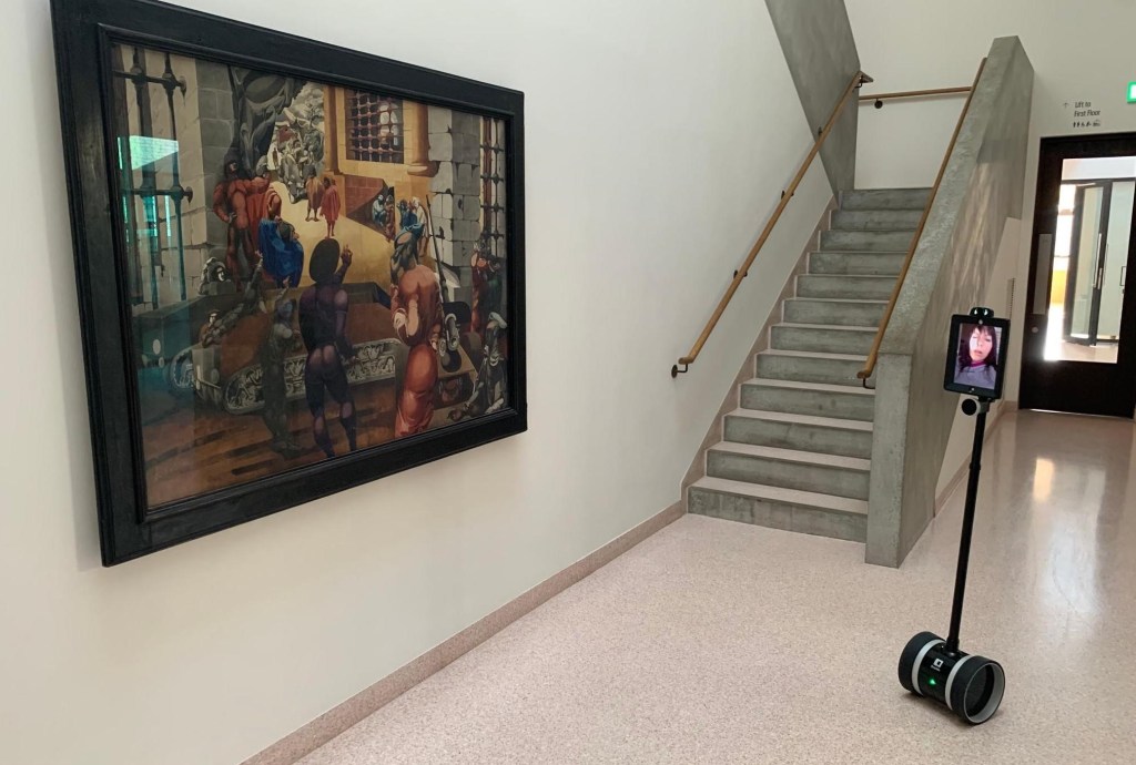 A tablet computer on a wheeling robot stopped in front of a painting, with a person visible on the tablet screen