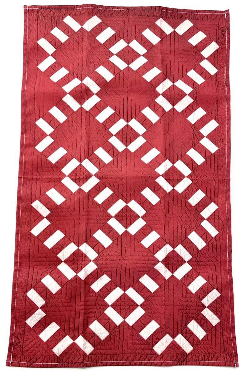 A quilted red tea towel with a white geometric pattern