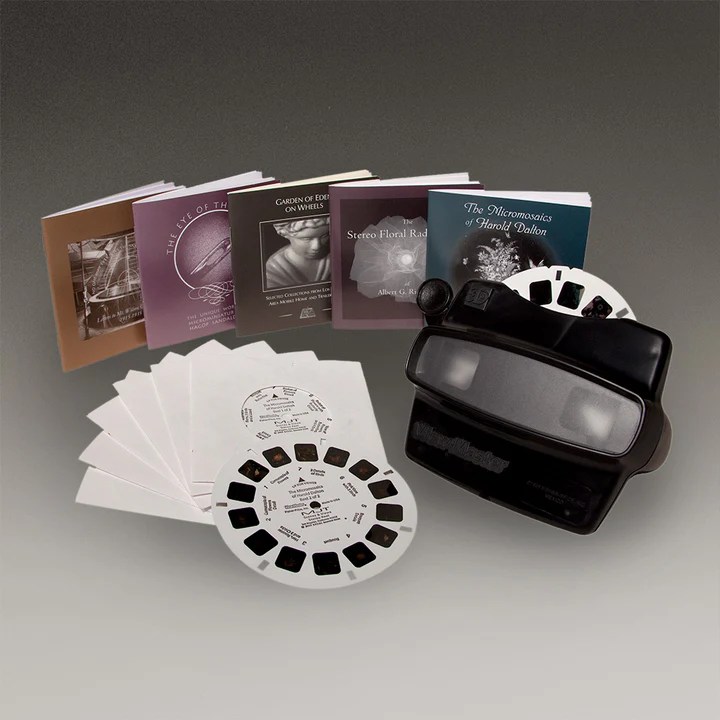 A black viewmaster toy with a stack of viewing cards and booklets on different subjects